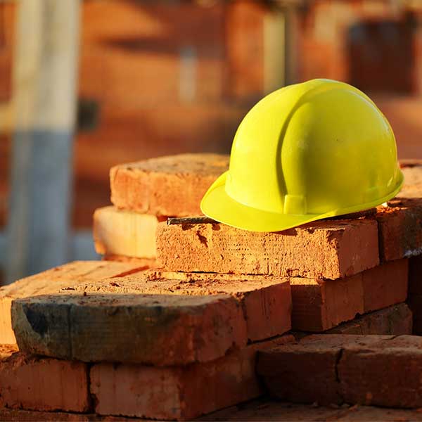 Servicio Construcción y Albañilería Casco amarillo colocado sobre unos ladrillos, simbolizando la seguridad en el trabajo de construcción.